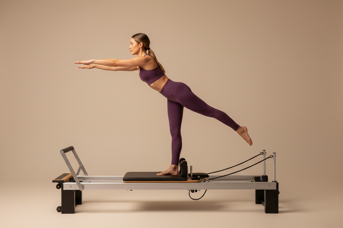 Woman in solid deep plum purple high-compression matching activewear set performing a standing balance extension on a Pilates reformer machine in warm studio lighting